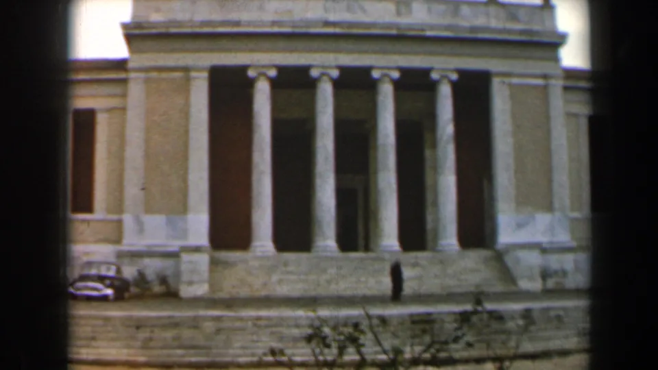 1960 Israel exterior of a grand columned building, with a parked mid-century car and a small pedestrian figure near the entrance steps.