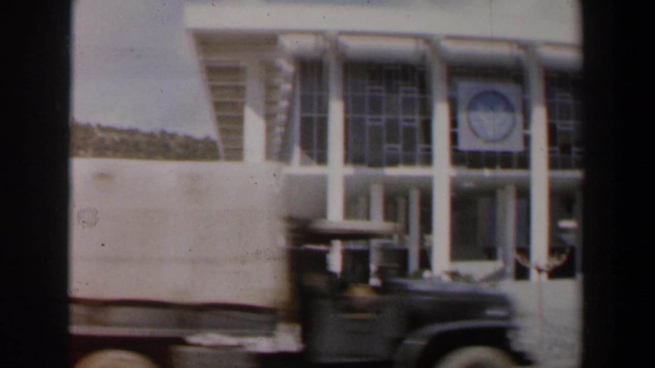 White modernist building partly obscured by a passing truck.