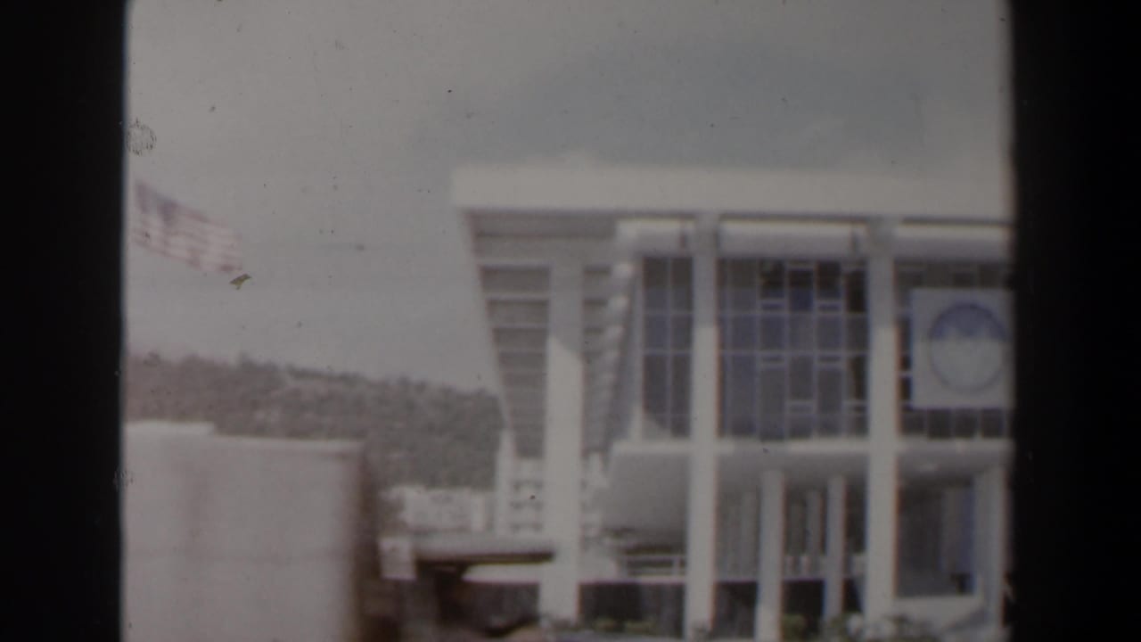 White columned building with emblem and hillside behind it.