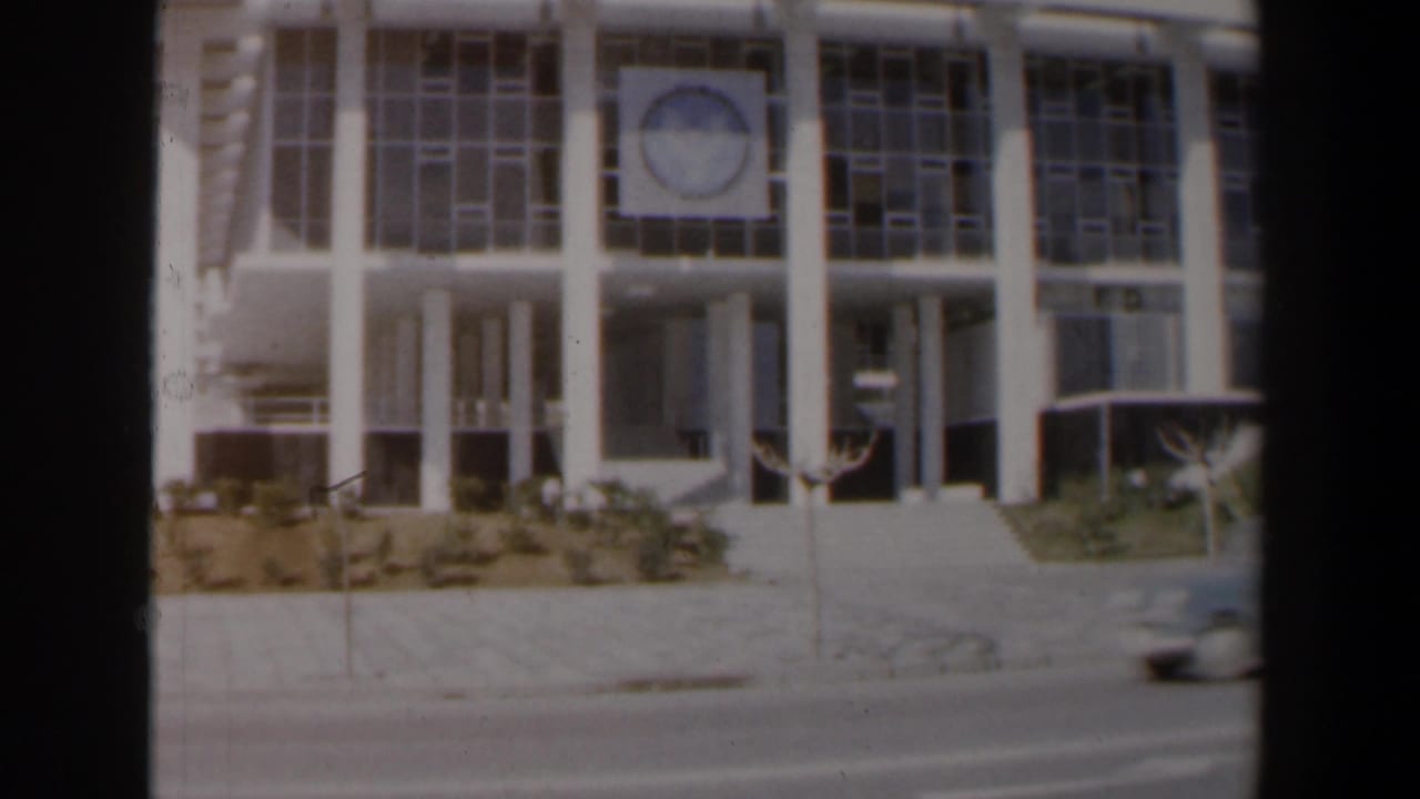 1960 Israel street view of a modernist institutional-looking building with columns, gridded windows, sidewalk, and roadway.