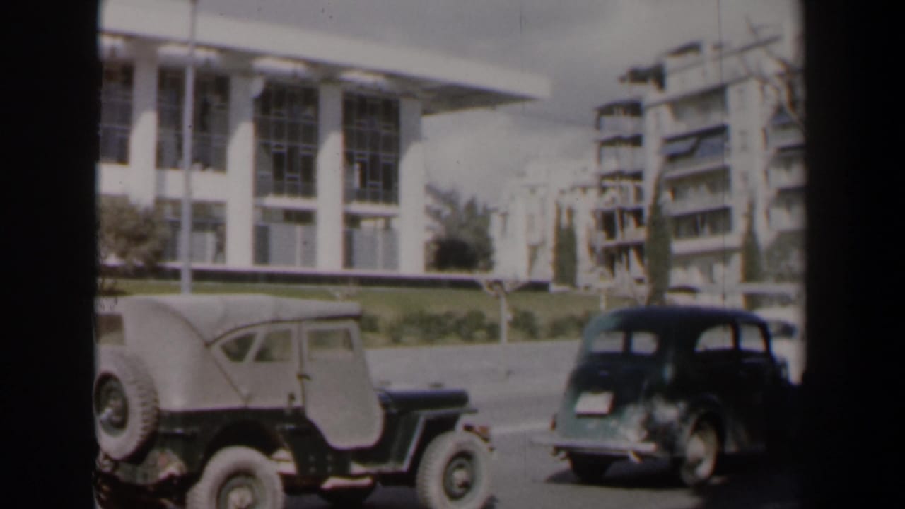 Two vintage vehicles parked on a street beside a white building with tall windows.
