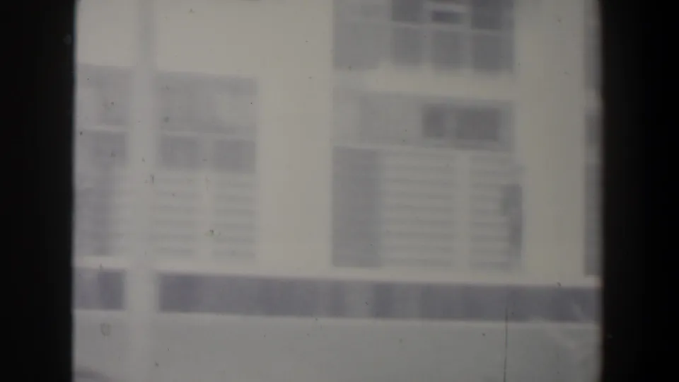1960 Israel home-movie frame showing a closer soft-focus view of a white building with gridded windows and dark horizontal trim.