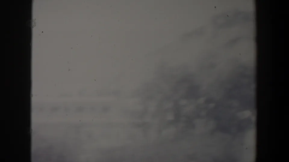 1960s Israel 8mm frame showing a soft, hazy hillside view through dark vertical divisions, with indistinct distant buildings.