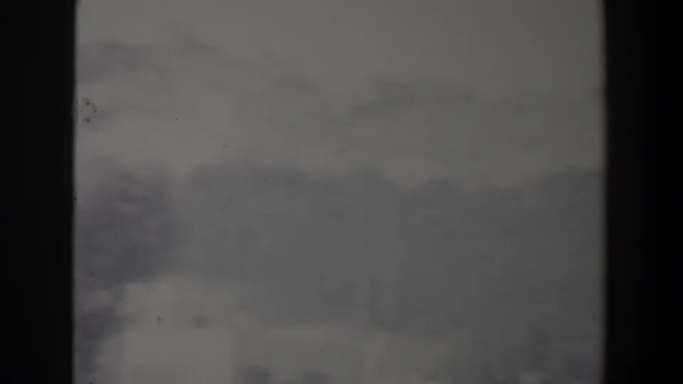 Soft 8mm view of a hazy Israel ridgeline with pale structures in the distance and dark foreground framing.