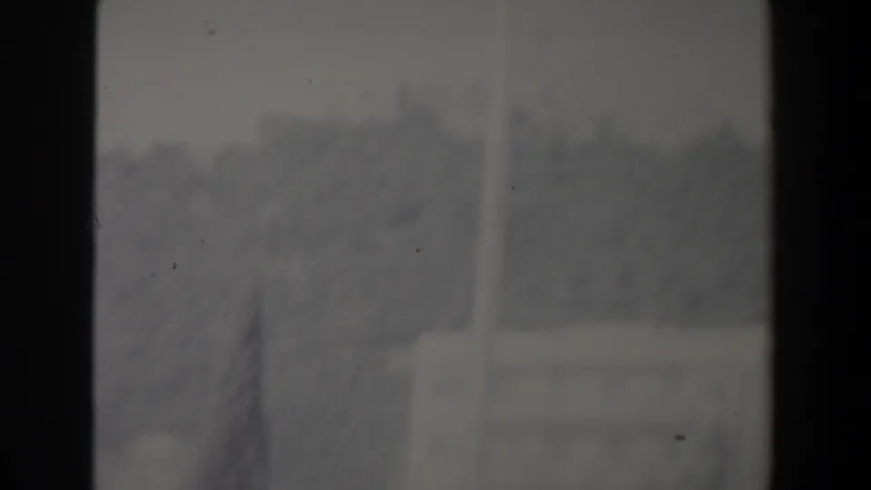 Soft 8mm frame from Israel showing a hazy hillside town area with pale buildings and a possible road or pole-like vertical line.