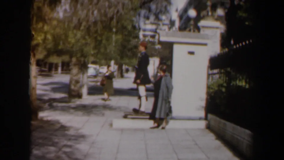 1960 Israel street frame with a stationary guard, woman near the sentry box, and a background pedestrian on the sidewalk.