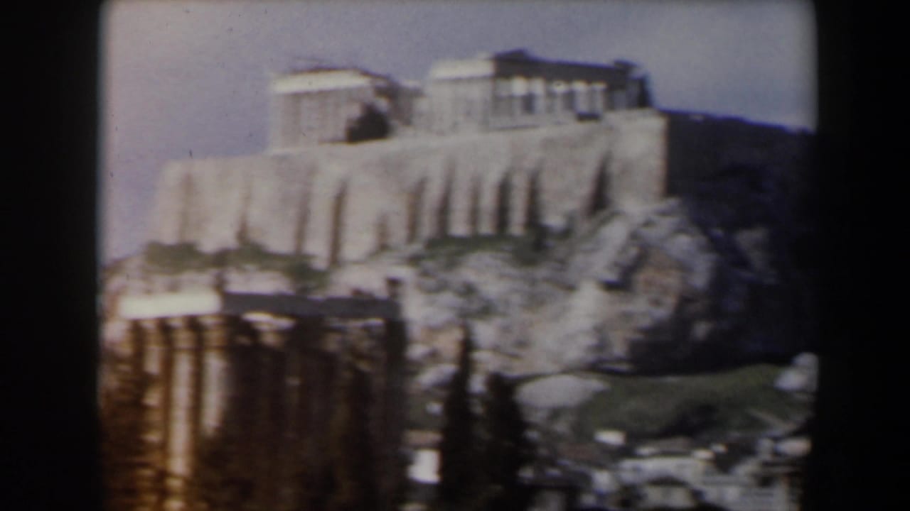Soft 8mm view of pale stone buildings on a rocky hill with ruins in the foreground.