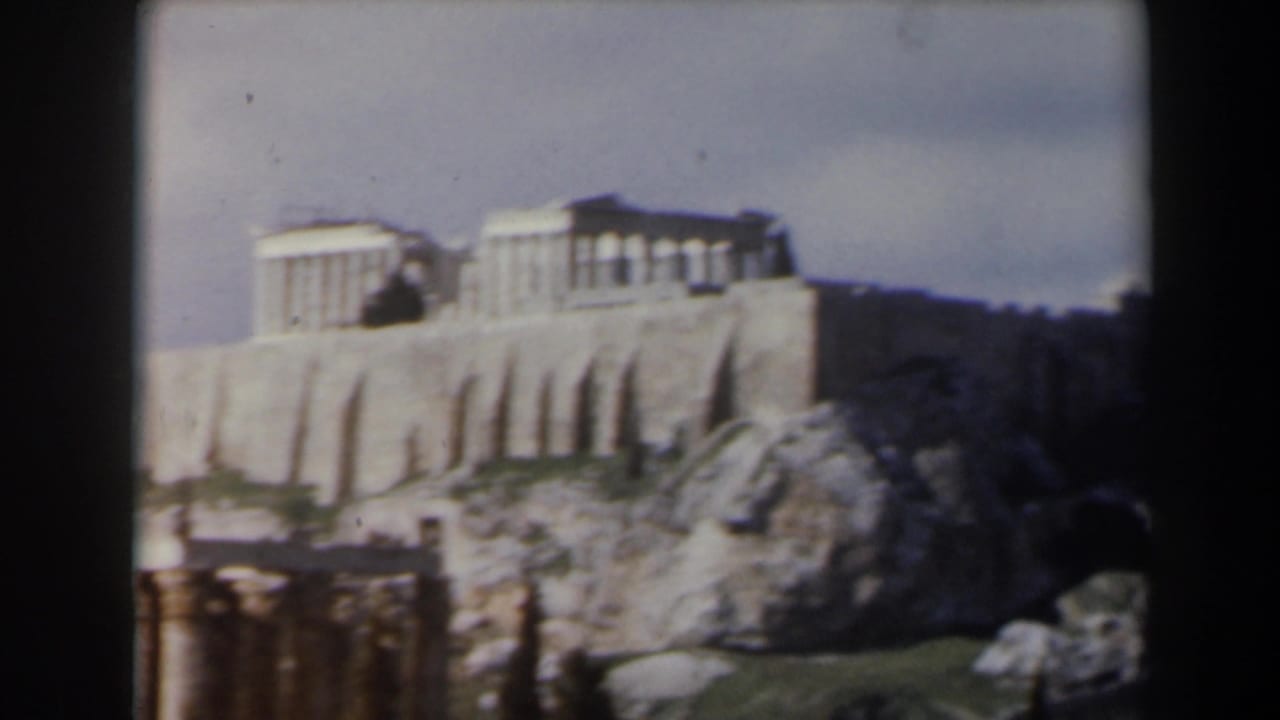 Distant temple columns on a rocky hill with pale retaining walls and ruins below.