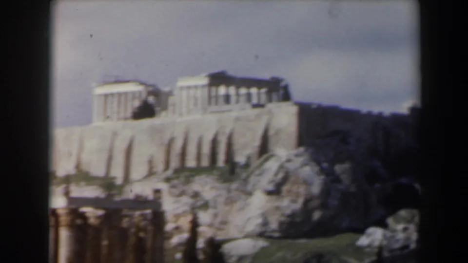 1960s 8mm travel frame showing an Acropolis-like temple complex on a rocky ledge under a bright sky.