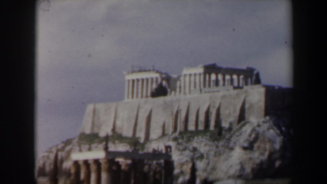 Columned temple buildings on a high stone ledge with rocks and ruins below.
