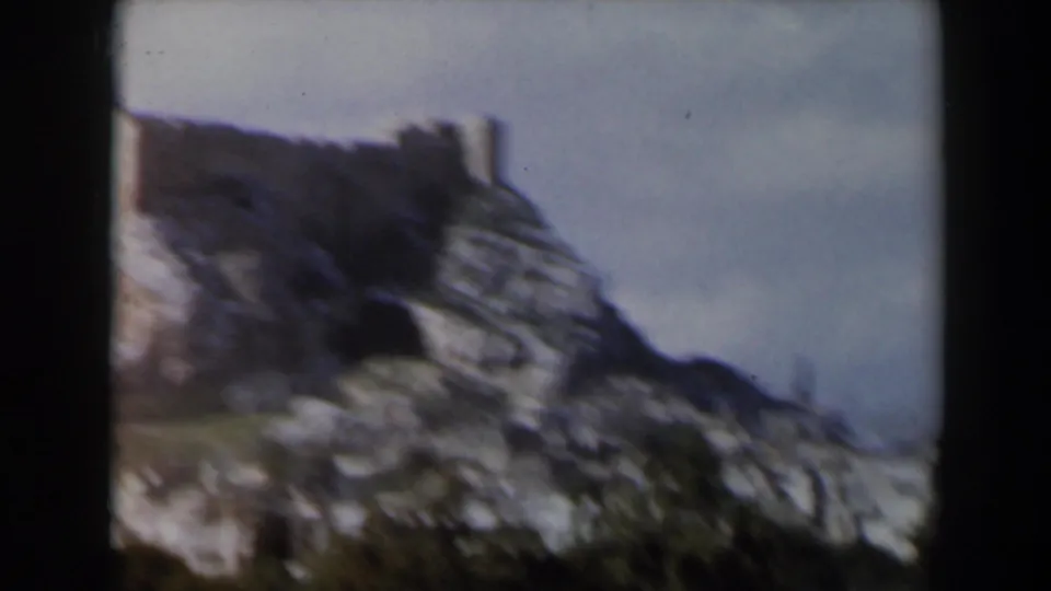 Soft 8mm frame of a rugged hill and small ruin fragment, shifting away from the main temple view.