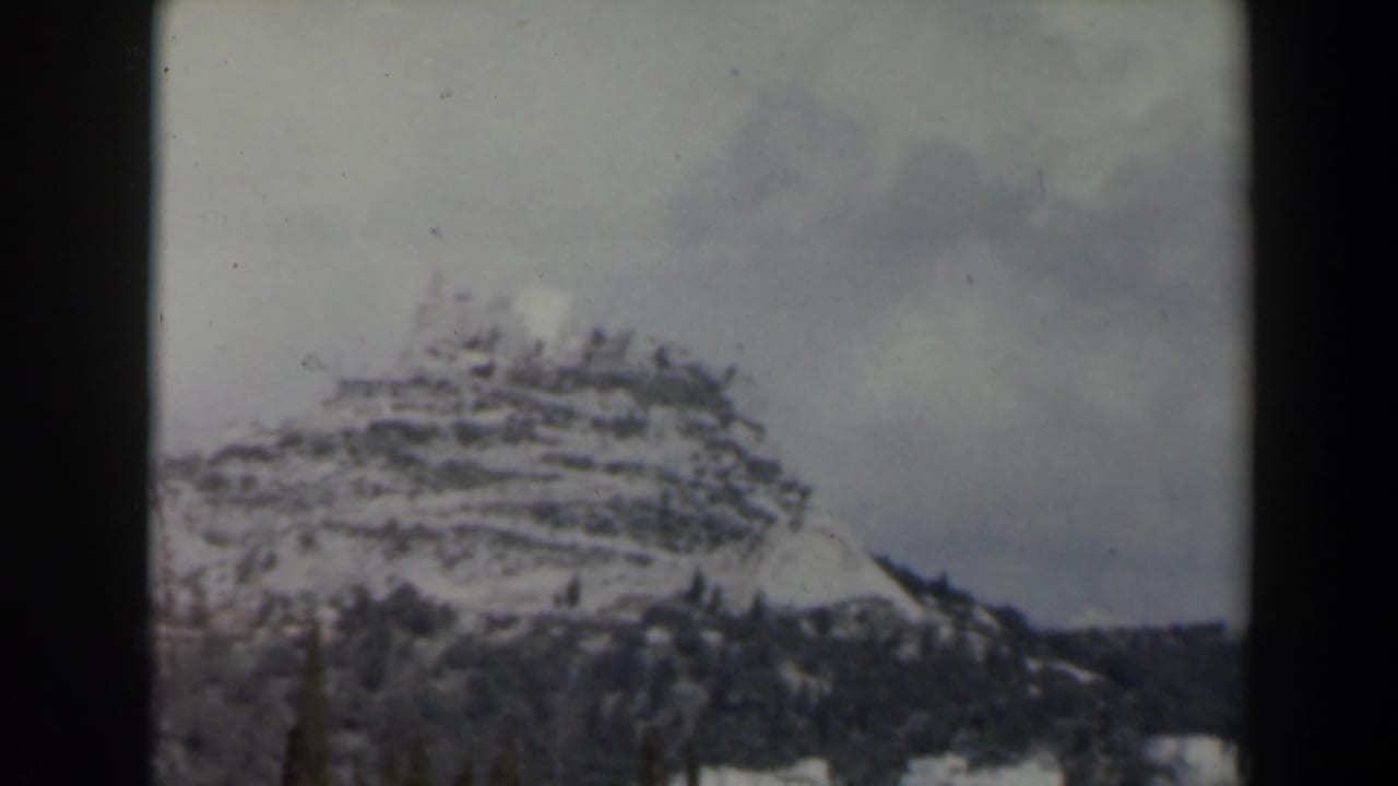 Snow-dusted terraced mountain ridge with dark trees beneath a cloudy sky.