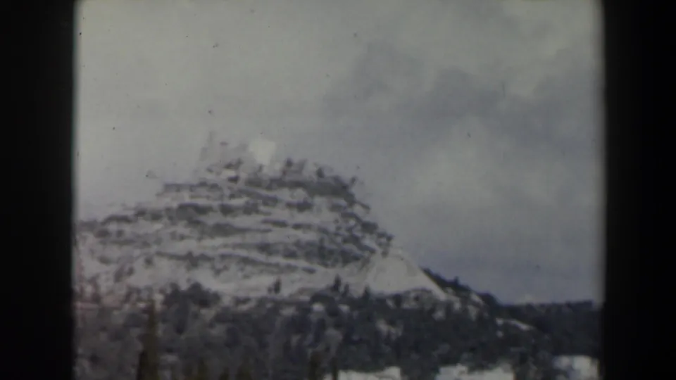 1960s Israel 8mm frame of a terraced snowy ridge with scattered pines and cloudy winter light.