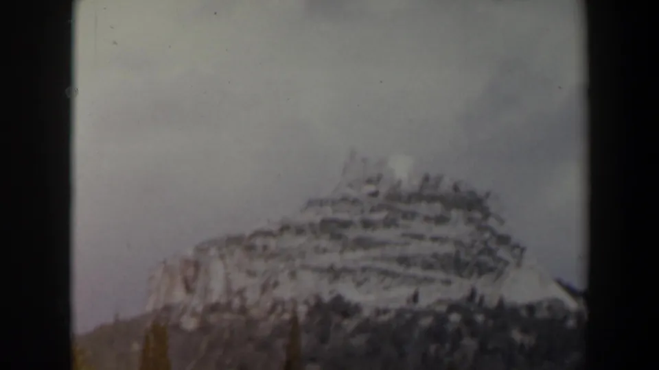 1960s Israel 8mm frame showing a closer snowy mountain face, terraced contours, and dark trees along the lower slope.