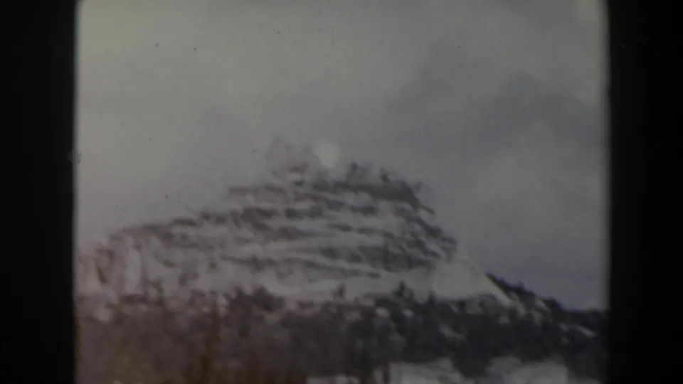 1960s Israel 8mm frame with a soft-focus snowy ridge, terraced hillside lines, pines, and gray winter sky.