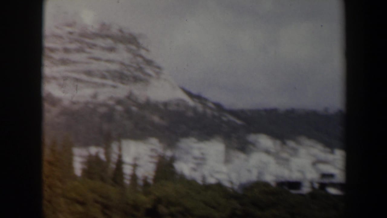 Snowy hillside with trees and white buildings under a cloudy sky.