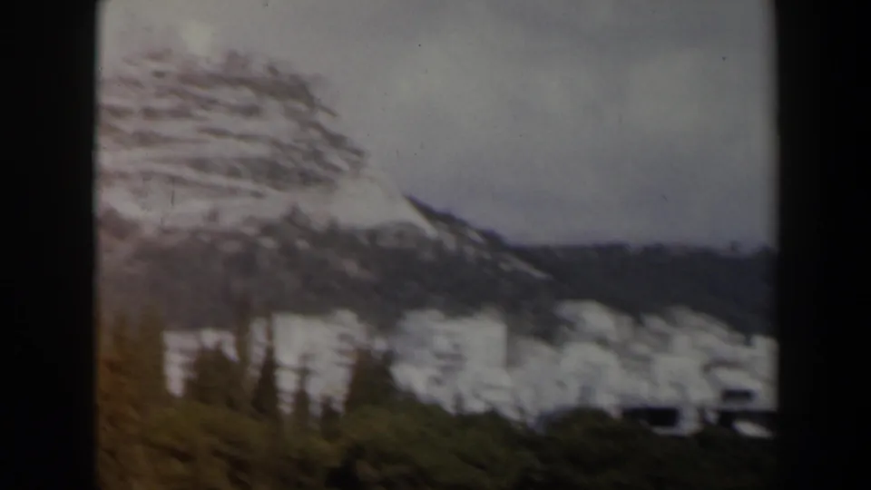 1960 Israel 8mm frame showing a snow-streaked hillside, dark green trees, and white buildings beneath clouds.