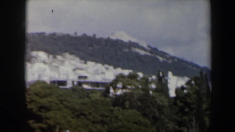 1960 Israel 8mm frame with snow on the hillside, pale buildings along the slope, and dense trees in the foreground.