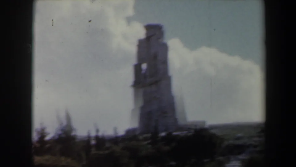 1960 Israel 8mm frame showing a tall weathered stone tower silhouetted against clouds and pale blue sky.
