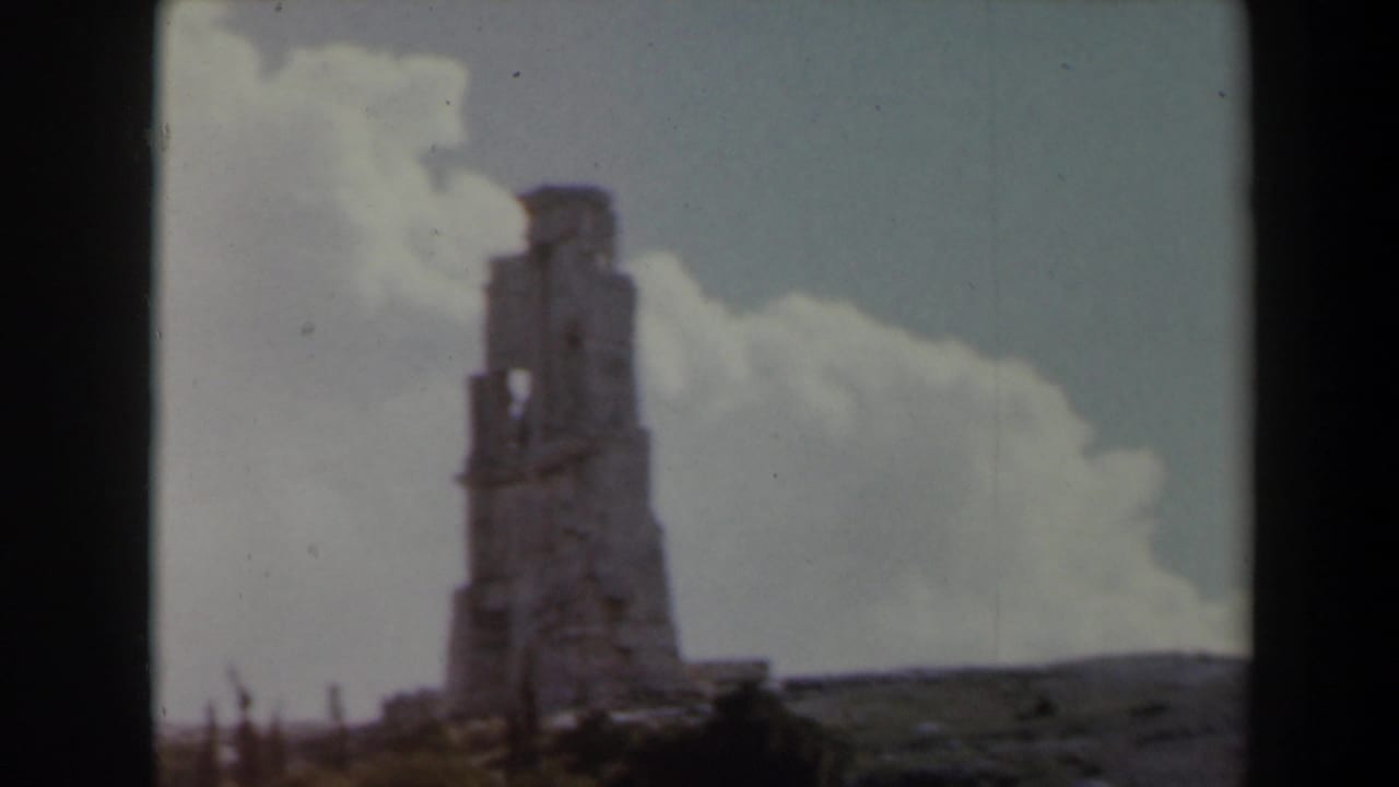 Stone ruin on a hill under clouds with dark foreground vegetation.