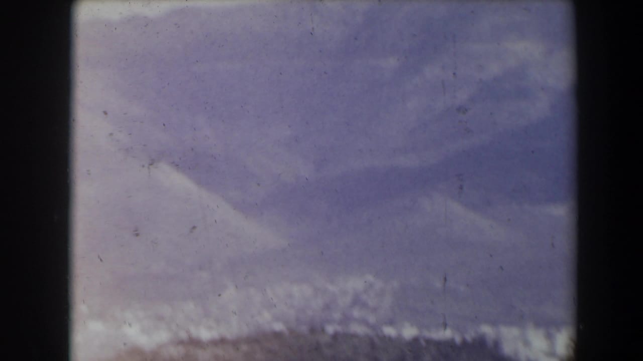 Soft, distant view of pale buildings below a hazy mountain ridge.