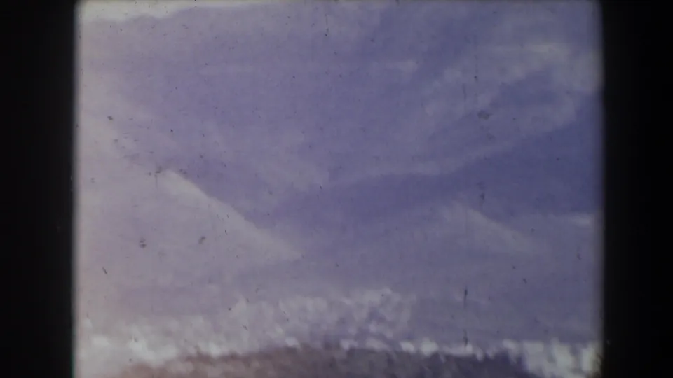 1960 Israel 8mm frame showing a blurred hillside town beneath a large hazy mountain ridge.