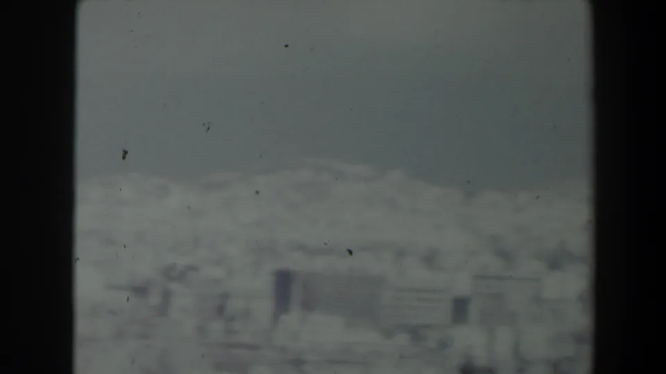 1960 Israel home-movie frame with white hillside structures and a muted mountain backdrop.