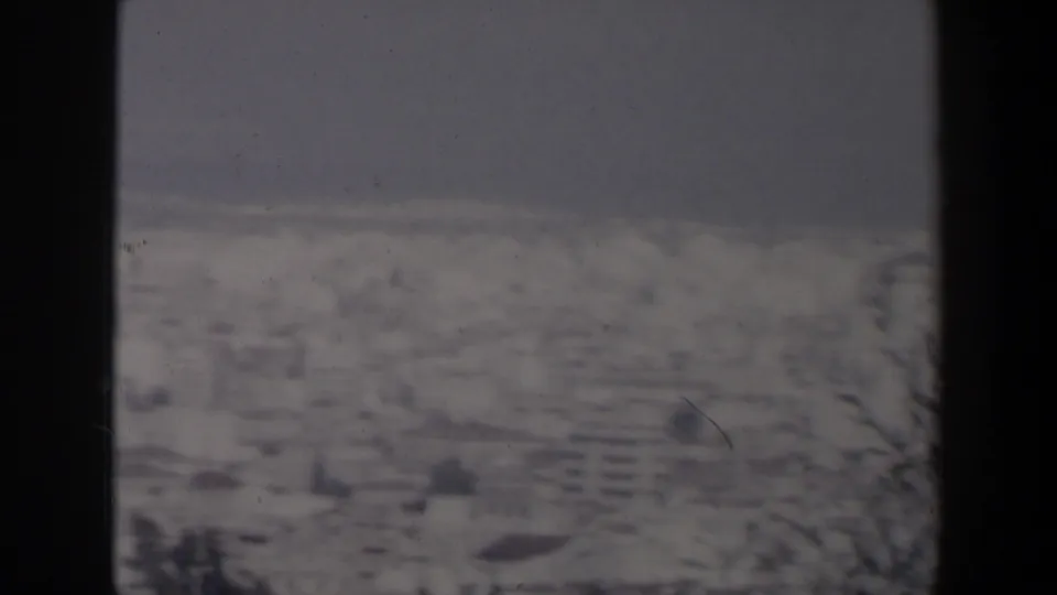 1960 Israel home-movie frame showing a soft distant coastal city, pale sea, muted sky, and dark film-frame borders.