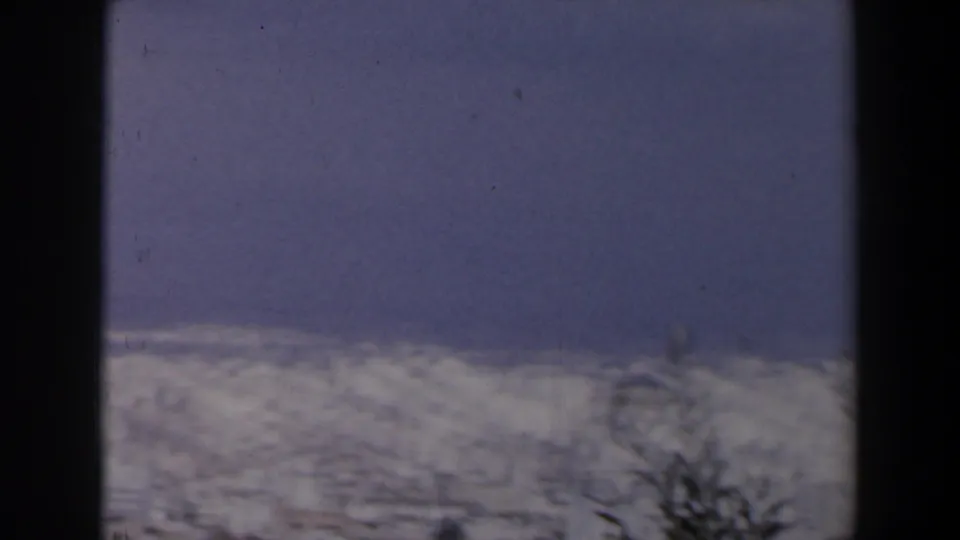 1960 Israel home-movie frame showing blue-gray sky, a pale coastal city, faint trees, and dark 8mm frame edges.