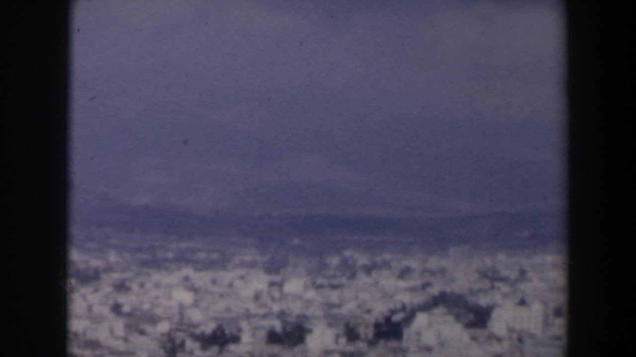 1960 Israel 8mm frame showing a hazy urban panorama beyond dark gate edges and distant hills.