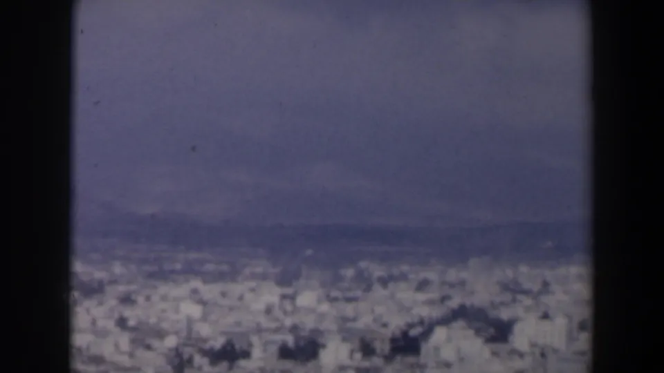 1960 Israel 8mm frame showing a hazy urban panorama beyond dark gate edges and distant hills.