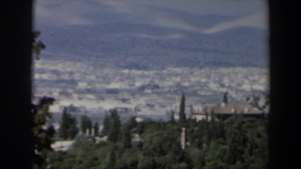 Hazy valley and hillside buildings seen through dark vertical frame borders.
