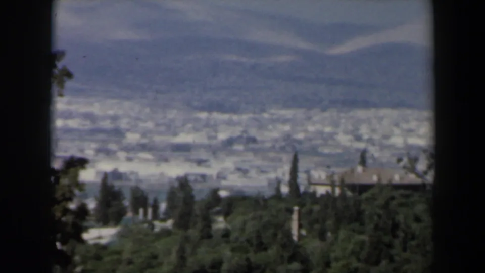 1960 Israel home-movie view of a hazy valley, hillside buildings and green trees through dark foreground borders.