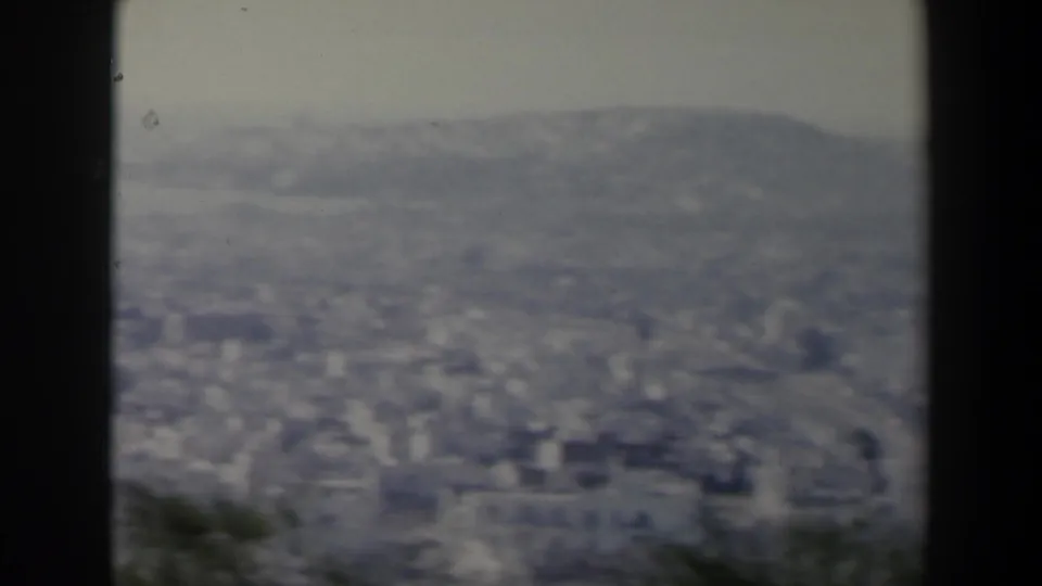 1960 8mm view in Israel showing a distant city below rolling hills, framed by dark gate edges and soft focus.