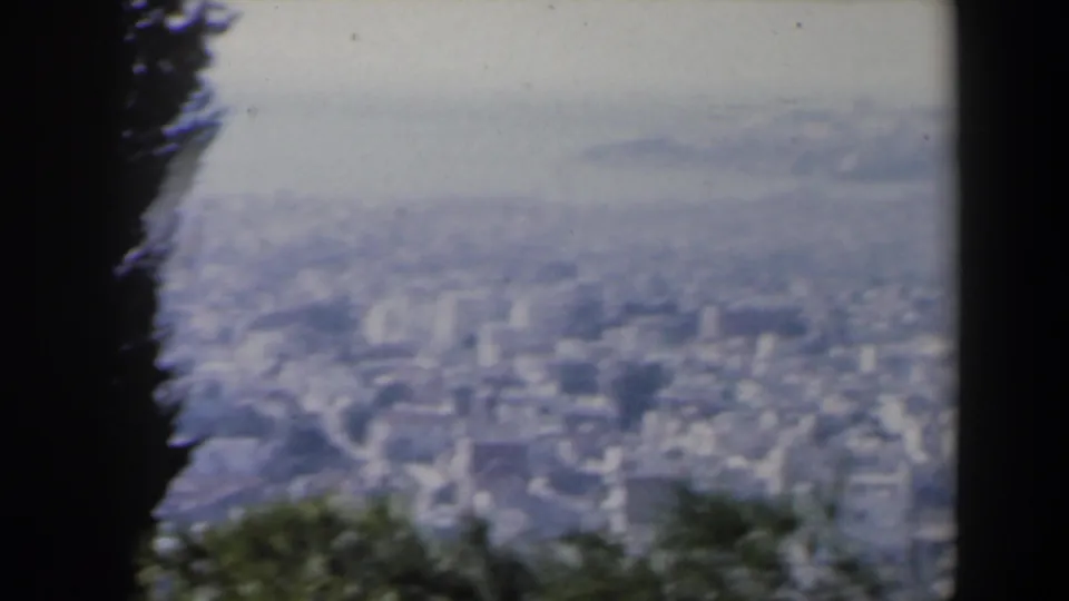 1960 Israel 8mm frame showing a hazy tan cityscape below foreground trees and a dark vertical framing element.