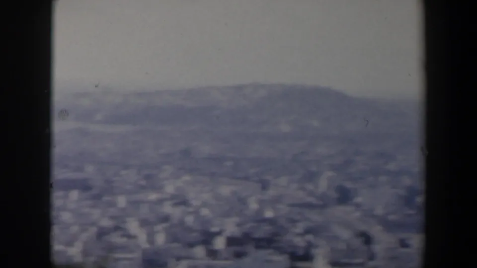 1960 Israel 8mm frame with a broad hazy urban panorama, hillside terrain, and dark foreground frame edges.