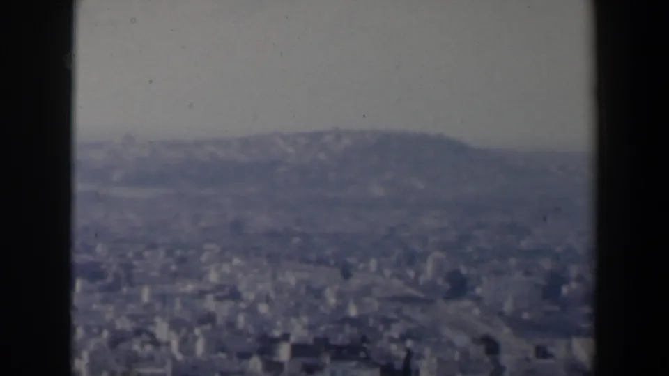 1960 Israel home-movie frame showing a hazy city panorama from a high viewpoint, partly framed by dark vertical edges.