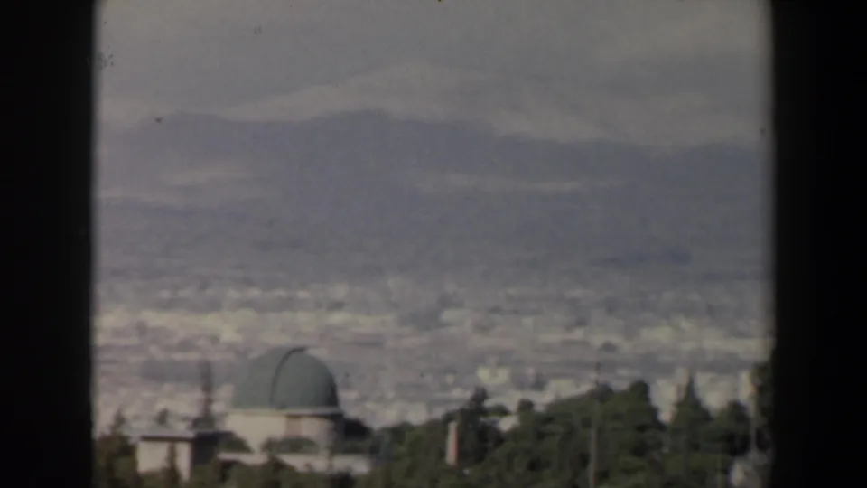 Elevated 1960 Israel home-movie frame showing a green-domed building, trees, distant city blocks, and hazy mountains.