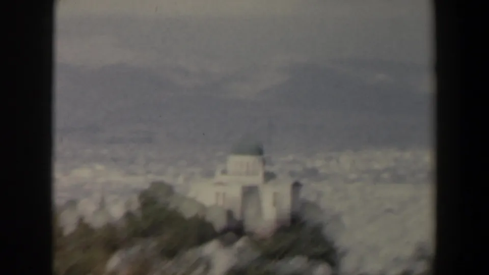 Soft-focused 1960 Israel frame with a pale domed structure on a green ridge and a hazy urban landscape beyond.