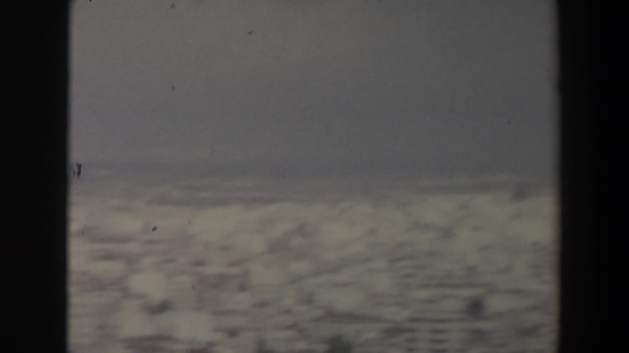 Hazy snow-covered mountain slope under a gray sky, divided by a dark vertical foreground band.