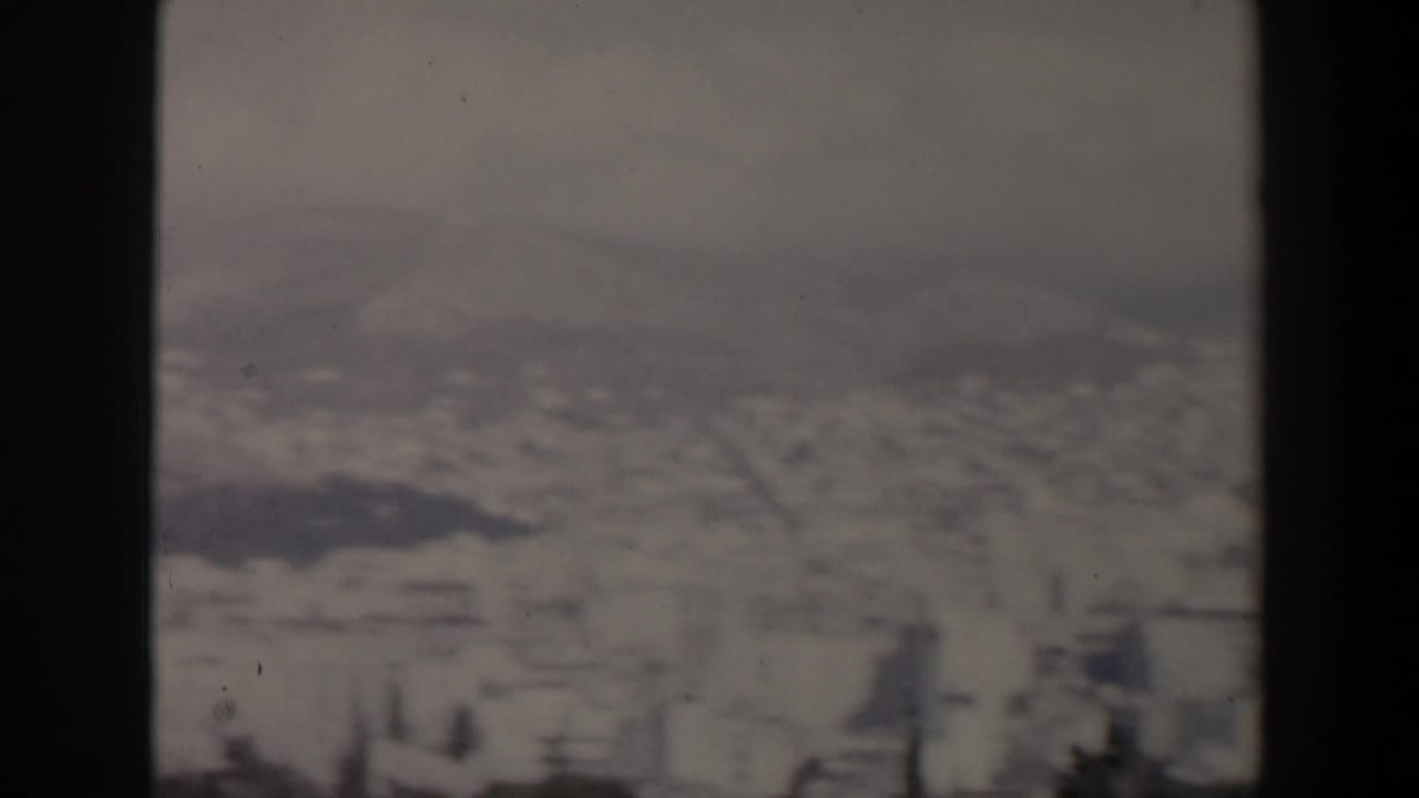 Blurred cityscape and hills behind a central dark film divider.