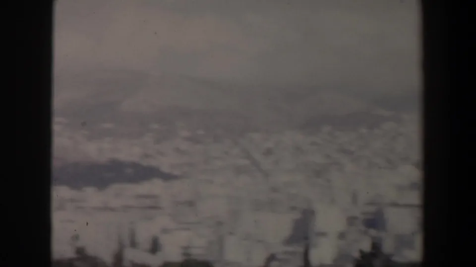 Soft 1960 Israel city view with distant buildings, low hills, and a dark vertical frame edge dominating the center.