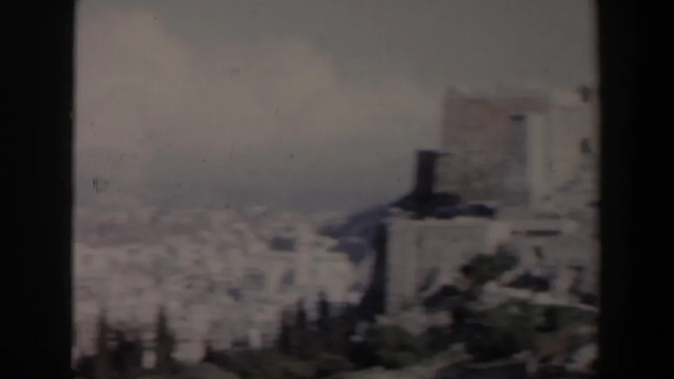 1960 Israel home-movie view of pale urban buildings with a darker tower-like form and foreground foliage at the lower edge.