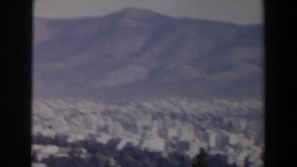 1960 8mm frame from Israel showing a hazy cityscape below low mountains, with soft focus and dark film borders.