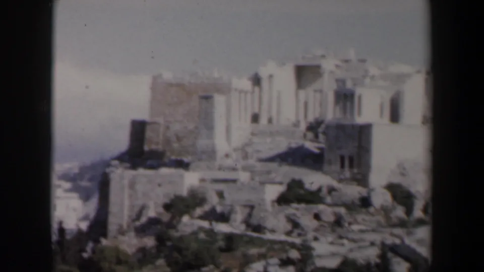 1960 8mm frame from Israel showing weathered stone ruins on a rocky rise under a pale, hazy sky.