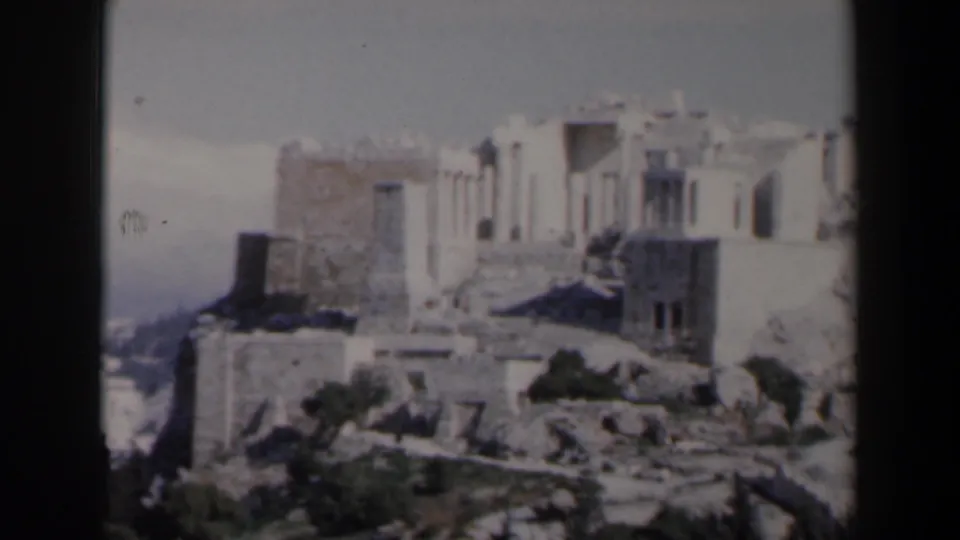 1960 8mm frame from Israel showing pale ruin walls, column-like forms, rocky terraces, and sparse vegetation.