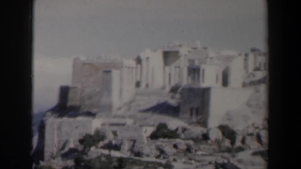 1960 8mm frame from Israel showing a softly focused hilltop ruin with stone walls, rocky foreground, and sparse plants.