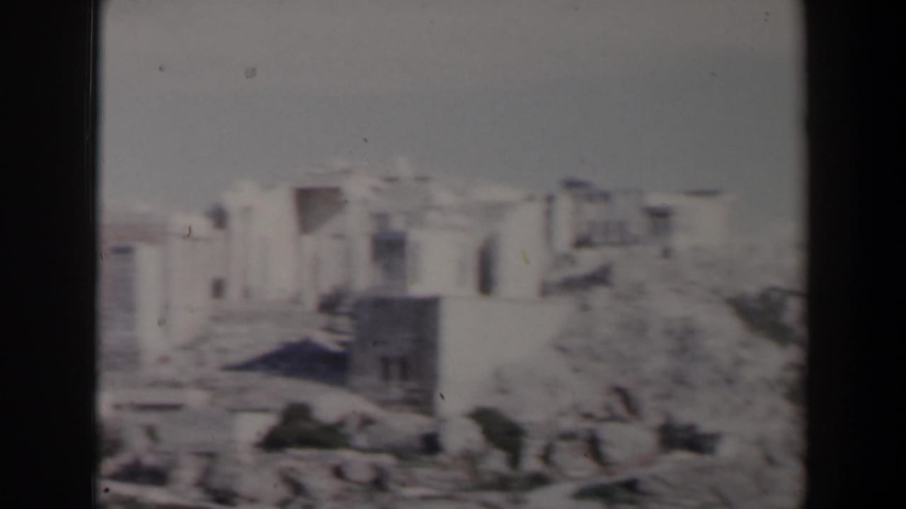 Distant pale stone buildings and ruins on a rocky hillside.