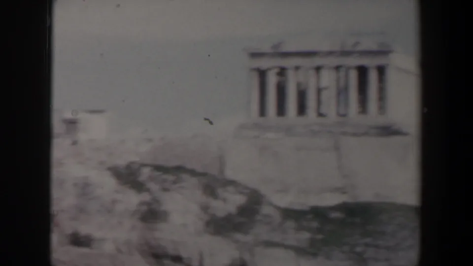 1960s Israel travel footage frame with a distant columned stone structure rising above rocks and pale masonry.