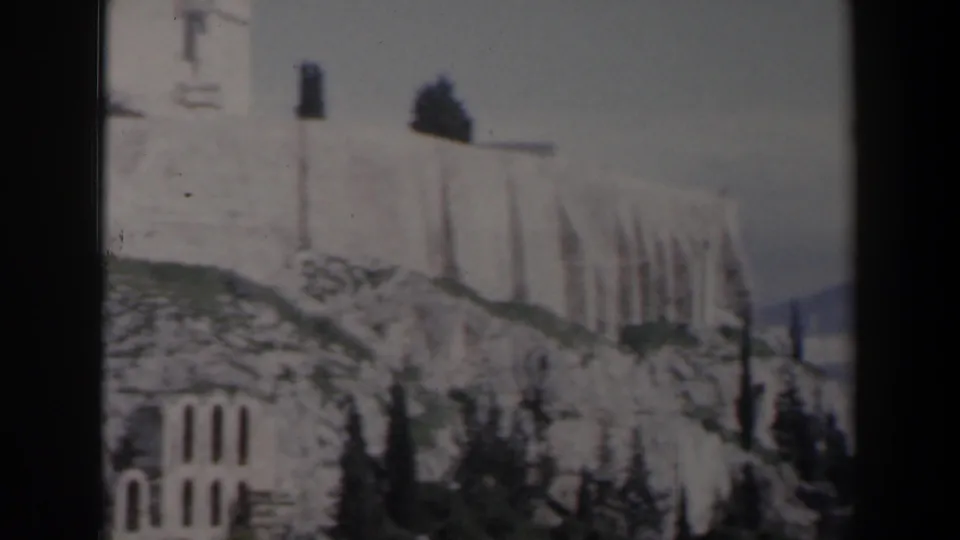 1960s 8mm frame from Israel showing stone walls, arched openings, rocks, and sparse trees near an ancient-looking site.